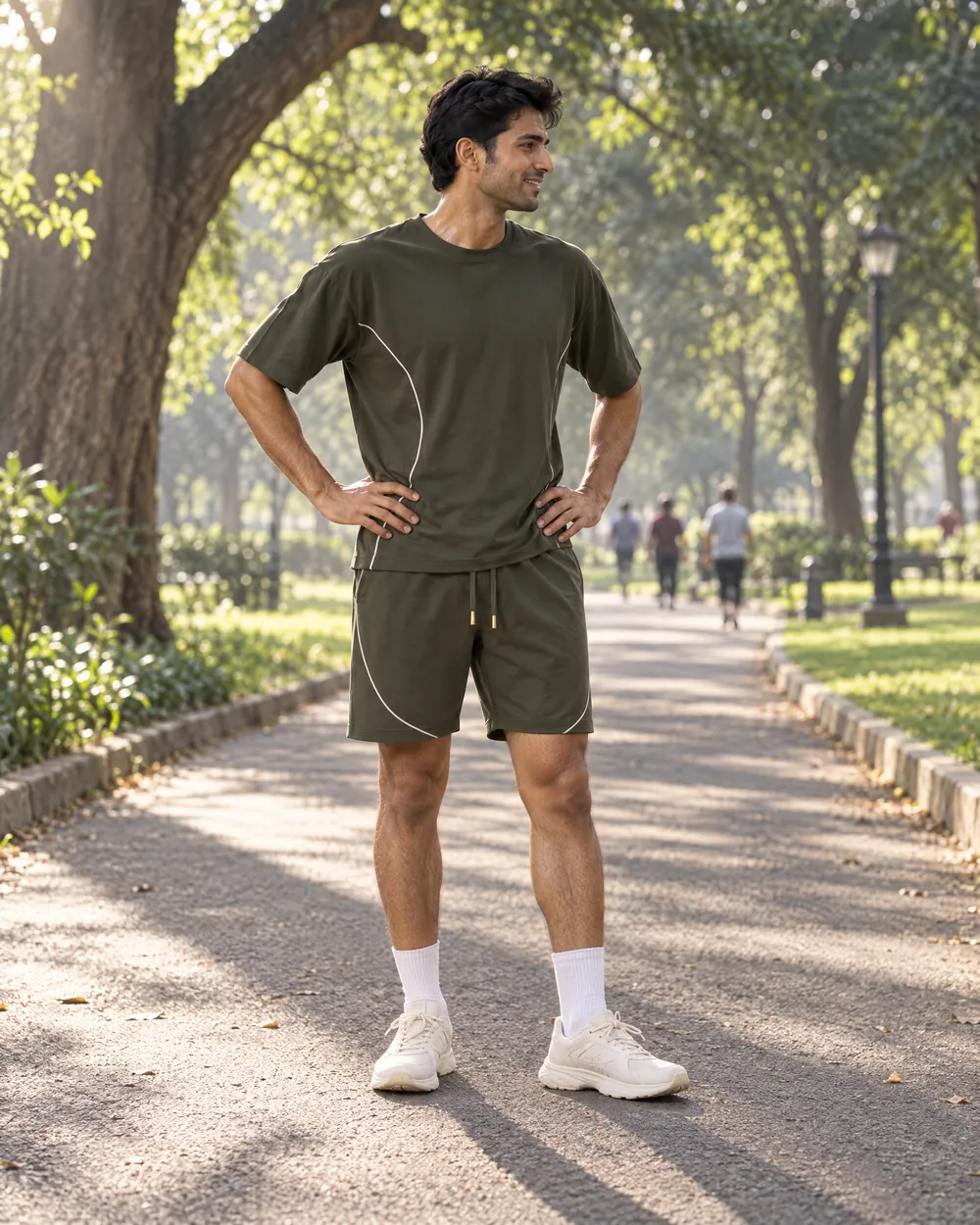 A man in an olive tee and shorts pausing mid-run in a park.