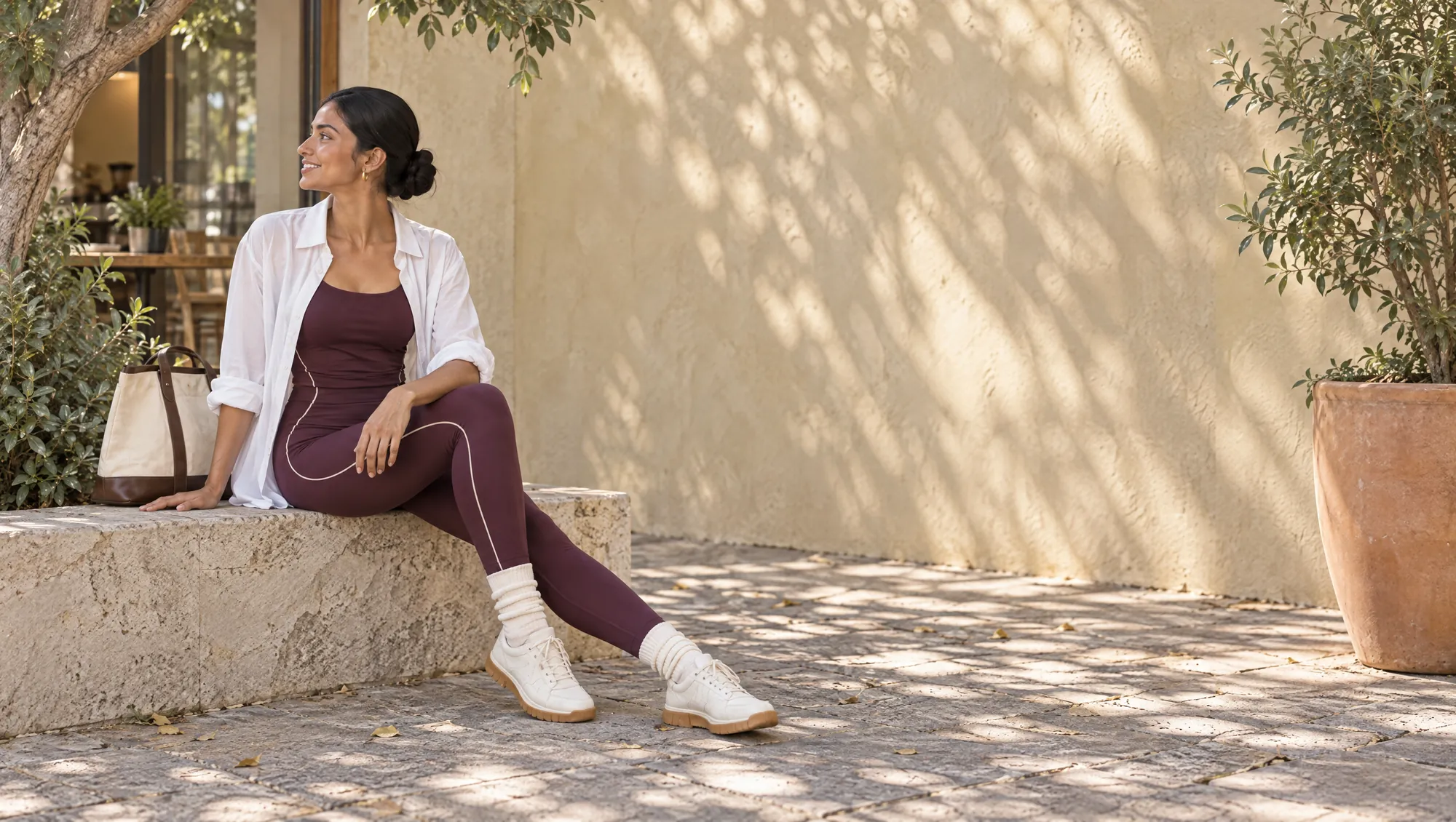 A woman in an aubergine tank and leggings with an open white shirt.
